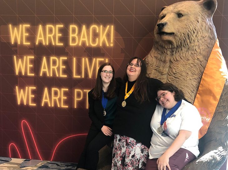 3 Students smiling in front of a bear statue